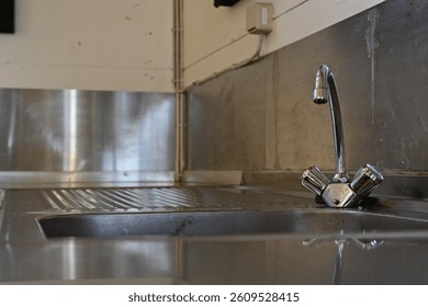 A close-up view of a stainless steel sink with a modern faucet and handles. The sink features a textured surface and is set against a plain wall, showcasing a minimalist design.