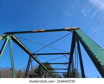 A closeup view of the steel beams that hold up a rusty old bridge. The bridge has a green overpass with lots of hazard signs for heavy or large vehicles attempting to pass through.