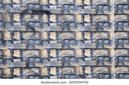 A closeup view of a stone wall, featuring roughhewn blocks in varying shades of grey and tan, creating a textured and natural pattern.