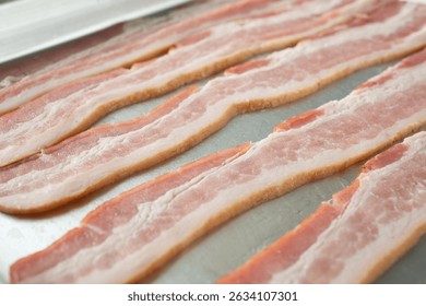 A closeup view of strips of raw bacon on a baking sheet.