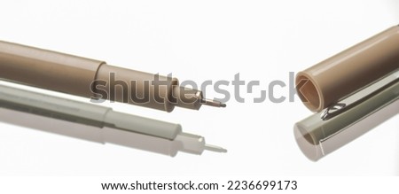 Close-up view of technical drawing pens in beige and gray with fine tips and removed caps on a white background, suitable for art, design, and drafting themes.