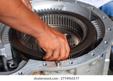 A close-up view of a technician's hands carefully assembling multiple clutch plates into a large industrial gearbox housing during a precision mechanical repair.