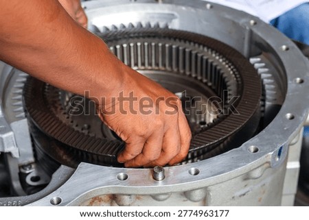 A close-up view of a technician's hands carefully assembling multiple clutch plates into a large industrial gearbox housing during a precision mechanical repair.