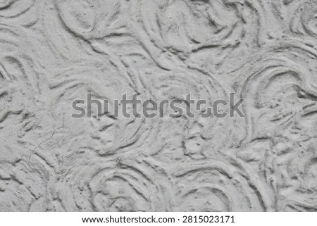 Closeup view of a textured light gray plaster wall featuring prominent, circular trowel swirl patterns.
