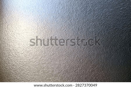 A close-up view of a textured metallic surface, showing subtle patterns and a bright light reflection.