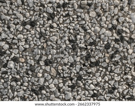 Close-up view of a textured surface composed of small gray and black pebbles, creating a rough and irregular pattern.
