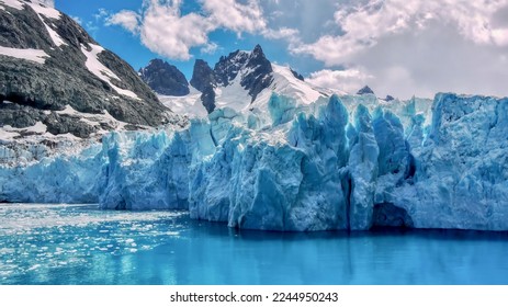 Closeup view of the textured surface of a glacier face, with jagged, snowcapped mountains in the background, in the Drygalski Fjord of South Georgia Island in the South Atlantic Ocean. - Shutterstock ID 2244950243