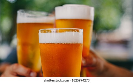 Close-up View Of A Three Glass Of Beer In Hand. Beer Glasses Clinking At Outdoor Bar Or Pub