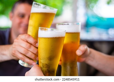 Close-up view of a three glass of beer in hand. Beer glasses clinking at outdoor bar or pub - Powered by Shutterstock