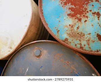 A close-up view of three weathered and rusty metal barrels, showcasing their textured surfaces, peeling paint, and varying colors in an abstract composition.