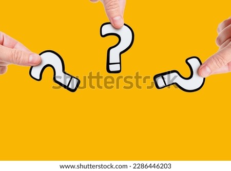 Close-up view of three white and black plastic question marks in hands isolated on plain yellow background with copy space. The concept of curiosity, inquiry and the search for answers.