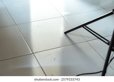 A close-up view of a tiled floor with reflections and a black metal chair leg partially visible in the corner.