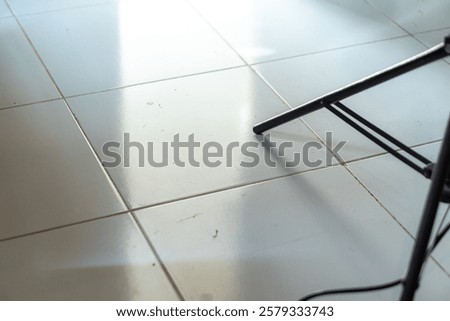A close-up view of a tiled floor with reflections and a black metal chair leg partially visible in the corner.