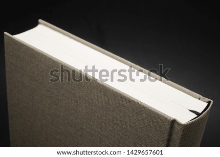 A close-up view of the top portion of a neutral-colored cloth-bound book with permanent black ribbon marker set on a slightly graduated and textured dark background.