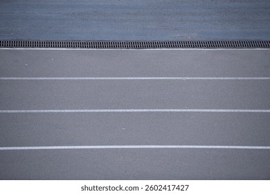 Close-up view of a track surface featuring clearly marked running lanes. The lines are white against the dark asphalt, highlighting the space ready for athletes to compete