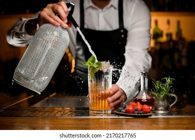 Close-up View Of Transparent Glass With Cold Cocktail Decorated With A Sprig Of Mint In Which Bartender Adds Carbonated Liquid From Siphon