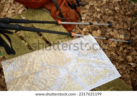 A close-up view of trekking poles and travel maps in the forest or mountains.