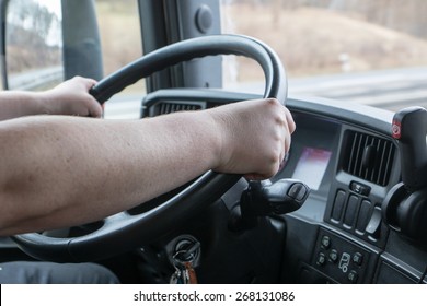 Closeup View From The Truck Cab. Truck Driver Keeps Driving Wheel With Both Hands.. Navigation Is Mounted On The Vehicle Dashboard. 