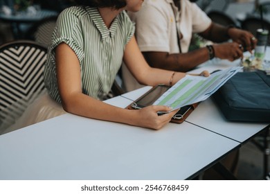 Close-up view of two colleagues reviewing papers during a business meeting. They are sitting at an outdoor cafe, focused on the documents. - Powered by Shutterstock