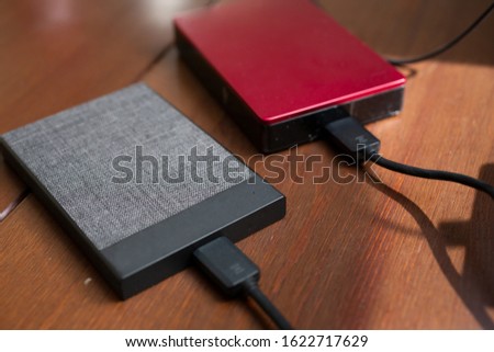 A closeup view of two external hard drives on a wooden table, connected to a computer with a cable.