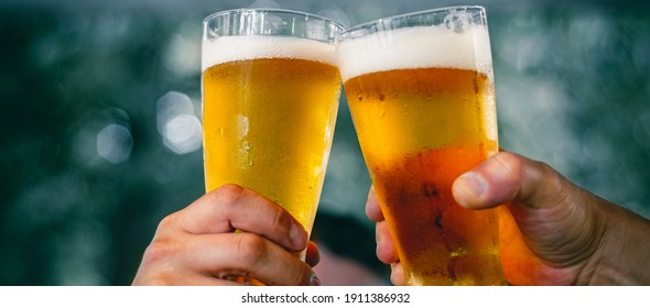 Close-up view of a two glass of beer in hand. Beer glasses clinking at outdoor bar or pub