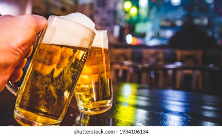 Close-up View Of A Two Glass Of Beer In Hand. Beer Glasses Clinking In Bar Or Pub