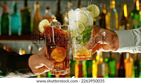 Close-up view of a two glasses of cocktails in hands. Cocktail glasses clinking at bar or pub.