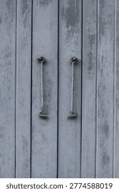 Close-up view of two old, gray metal doors featuring rustic hook and eye latches, showing signs of age and wear