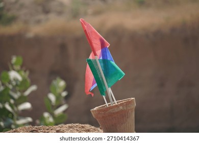 A close-up view of two small blank flags placed inside a decorative plant pot outdoors. The simple flags with plain colors create a minimal and modern visual composition.