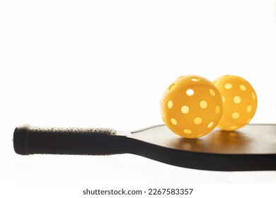 Closeup view of two yellow pickleballls on top of the black pickleball racket with glowing white background and copy space