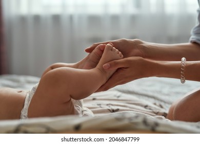 Closeup View Unrecognised Female Hands Holding Barefeet Baby's Legs. Connection Between Mother And Child. Skin Contact During Baby Massage Routine.