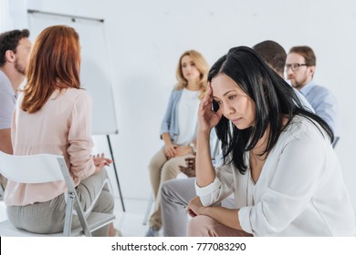 Close-up View Of Upset Asian Middle Aged Woman And People Sitting On Chairs Behind During Group Therapy