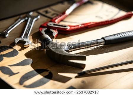 Close-up view of various hand tools, including a hammer, multi-grip pliers, a screwdriver, and flat wrenches, arranged neatly on a rustic wooden table.