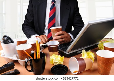 Closeup View Of A Very Cluttered Businessmans Desk. Man Is Holding A Coffee Cup And Crumpled Papers Litter His Workspace. HIgh Key Office Background.