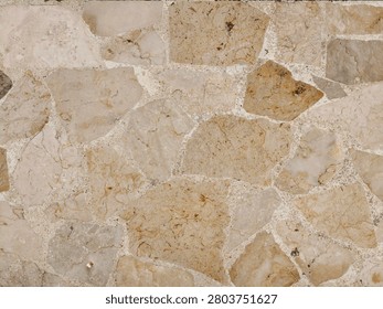 A close-up view of a wall constructed from irregularly shaped natural stones in various shades of beige and brown, creating a rustic and textured background.
