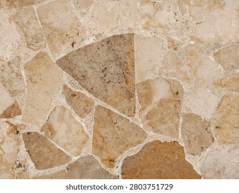 A close-up view of a wall constructed from irregularly shaped natural stones, showcasing a mosaic of earthy tones including beige, brown, and hints of pink.