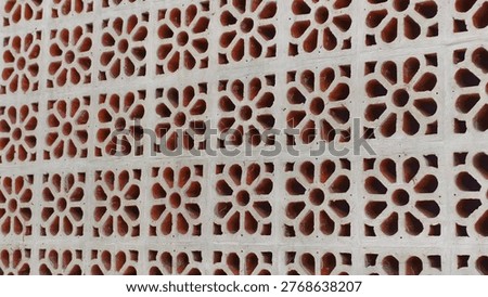 Close-up view of a wall made of white perforated concrete blocks featuring a repeating floral design.