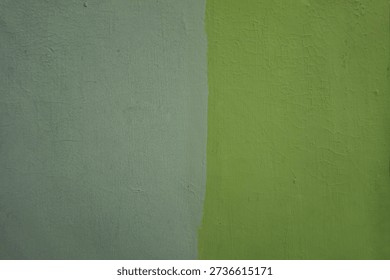 A close-up view of a wall painted in two distinct colors, a muted grey on the left and a vibrant lime green on the right, meeting in a sharp vertical line.