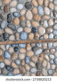 A close-up view of a wall or surface adorned with numerous smooth, colorful river pebbles and stones embedded in mortar, creating a natural and textured background.