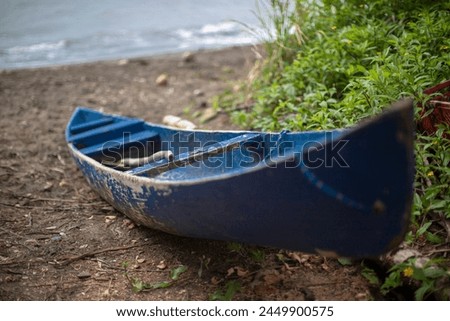 a close-up view of a weathered blue canoe resting on a sandy beach. The canoe shows signs of wear and the paint is peeling, indicating it has been used extensively, possibly for fishing or traveling a