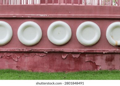 A close-up view of a weathered red structure featuring a repeating pattern of circular white embellishments and distressed paintwork