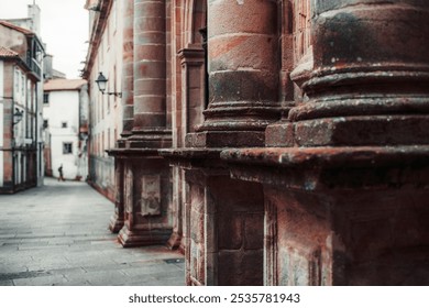 Close-up view of weathered stone columns on a historic building facade, showcasing detailed texture and architectural elements. A quiet narrow street fades into the background - Powered by Shutterstock