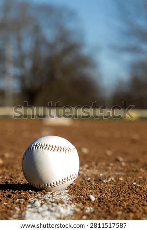A close-up view of a white baseball with red stitching sits on the infield dirt, ready for the game to begin