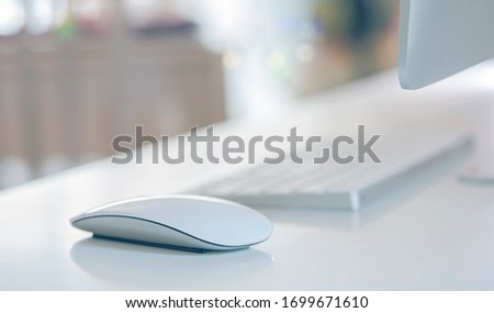 Closeup view of white computer mouse with keyboard and monitor on white table in modern house, shallow DOF.
