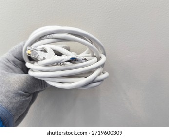 A close-up view of a white Ethernet cable with its outer sheath torn, revealing colored internal wires, held by a gloved hand against a textured wall background.