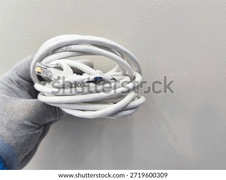 A close-up view of a white Ethernet cable with its outer sheath torn, revealing colored internal wires, held by a gloved hand against a textured wall background.