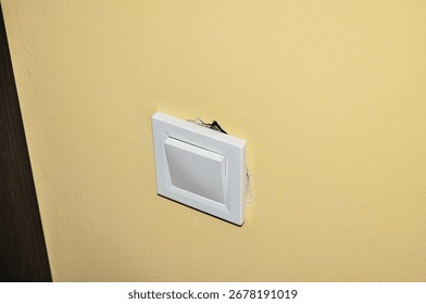 A close-up view of a white light switch on a yellow wall, showing signs of damage around the edges.