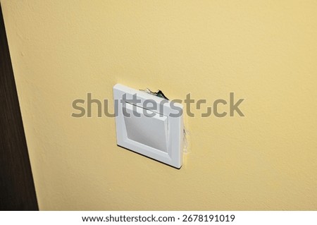 A close-up view of a white light switch on a yellow wall, showing signs of damage around the edges.