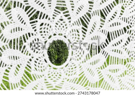 Close-up view of a white macrame hammock's detailed pattern, revealing blurred green grass and tree leaves underneath