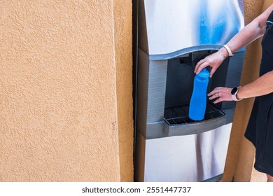 Close-up view of woman filling blue bottle with ice from dispenser machine on sunny warm day. Aruba. - Powered by Shutterstock